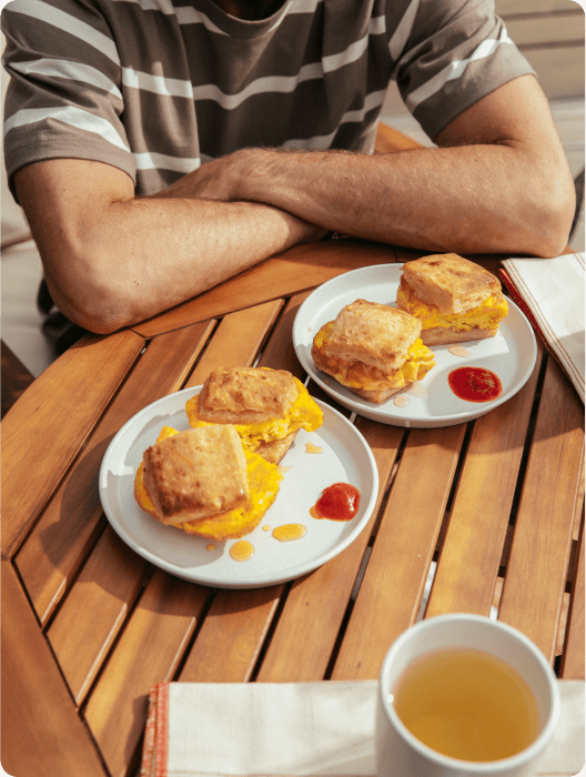 A man sitting with two egg and cheddar breakfast sandwiches on the table in front of him